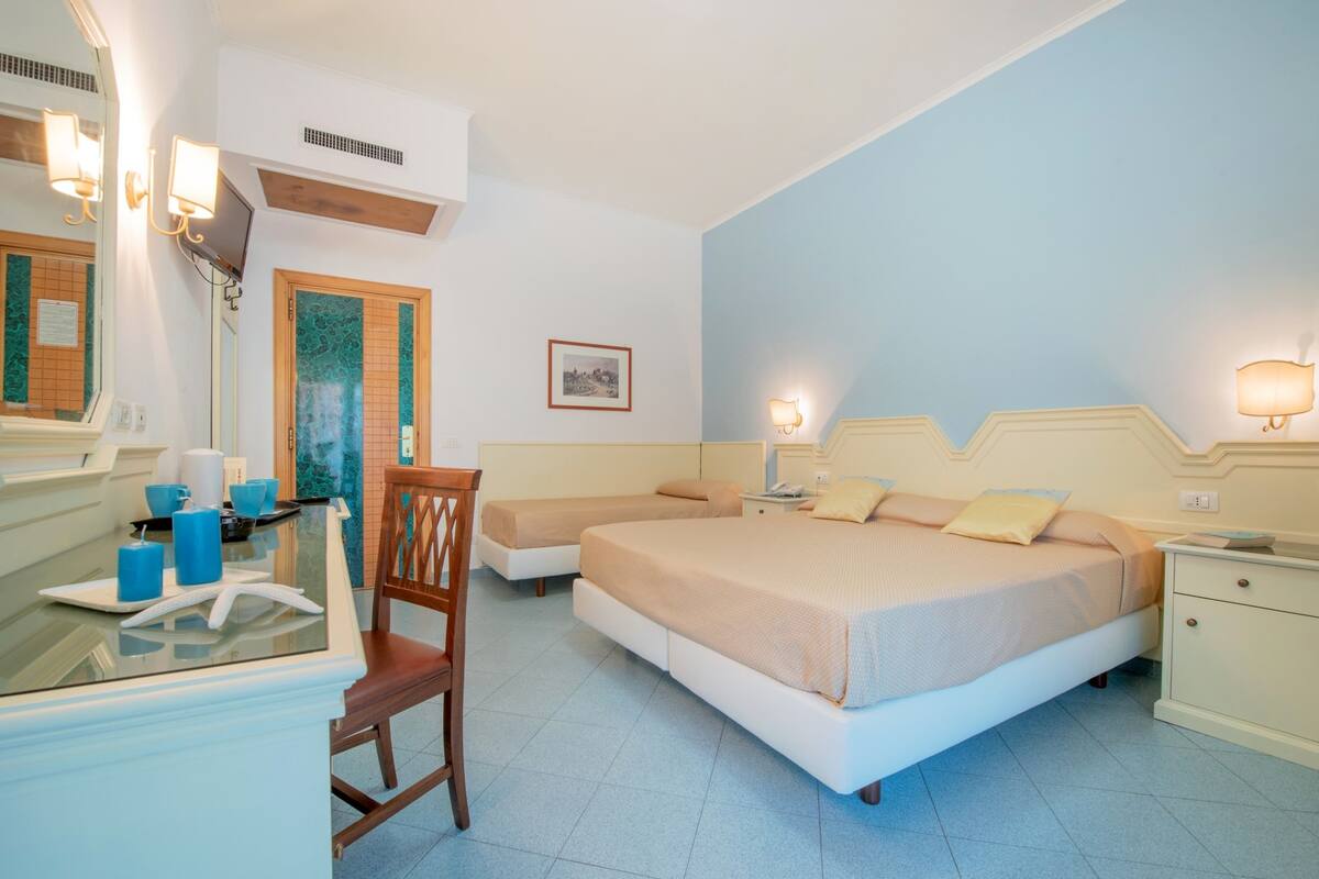 A bedroom with a bed, bedside tables, a chair, a desk with a mirror, and a small table with candles.