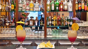 Un bar con dos bebidas, cada una decorada con una rodaja de naranja y una pajita, y un plato de patatas en el centro.