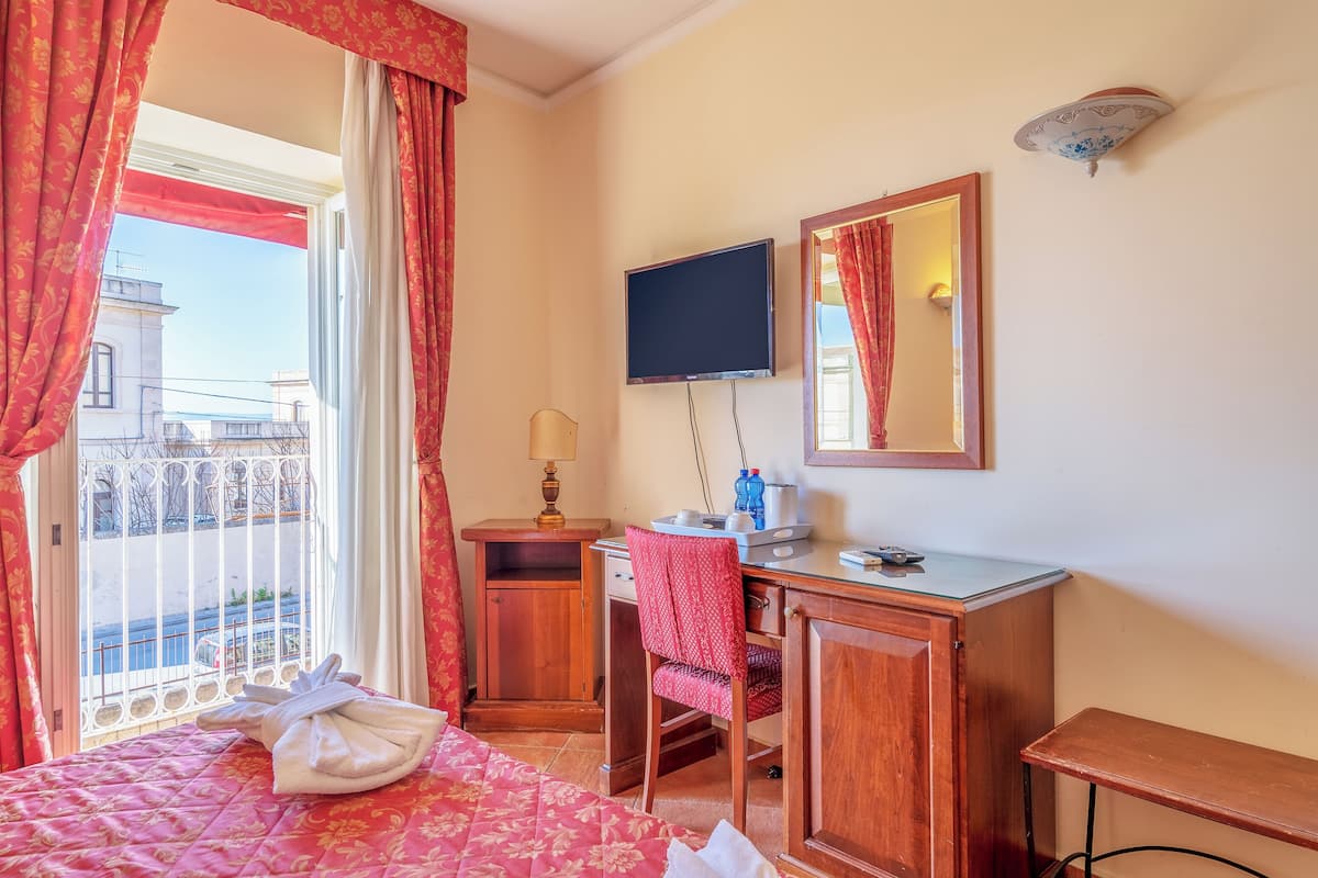A hotel room with a bed, a desk, a chair, a TV, and a window with curtains.