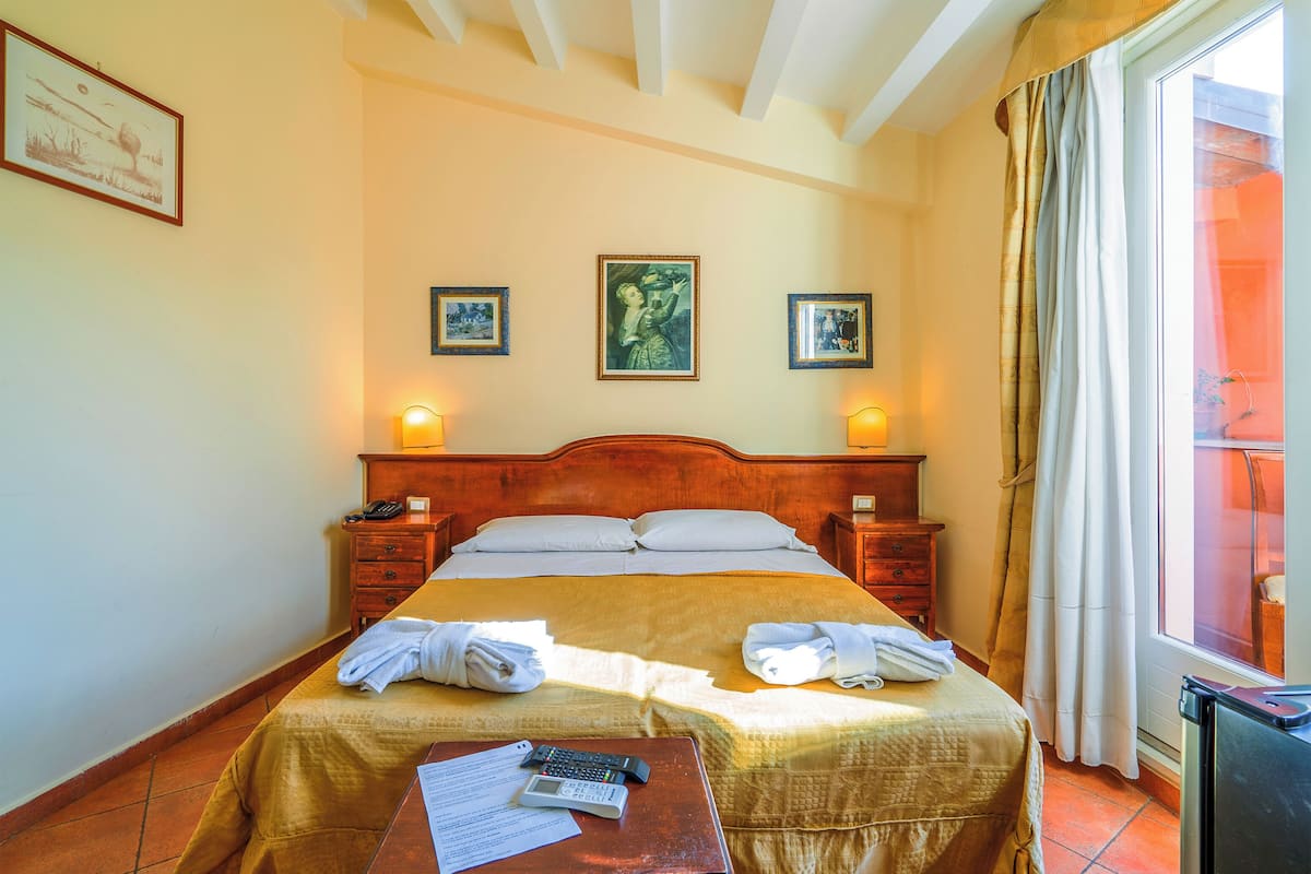 A hotel room with a bed, bedside tables, and a window with curtains.