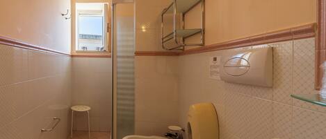 A bathroom with a shower, toilet, bidet, and a small stool.