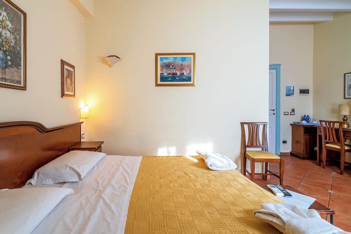 A hotel room with a bed, a desk, a chair, and a painting on the wall.
