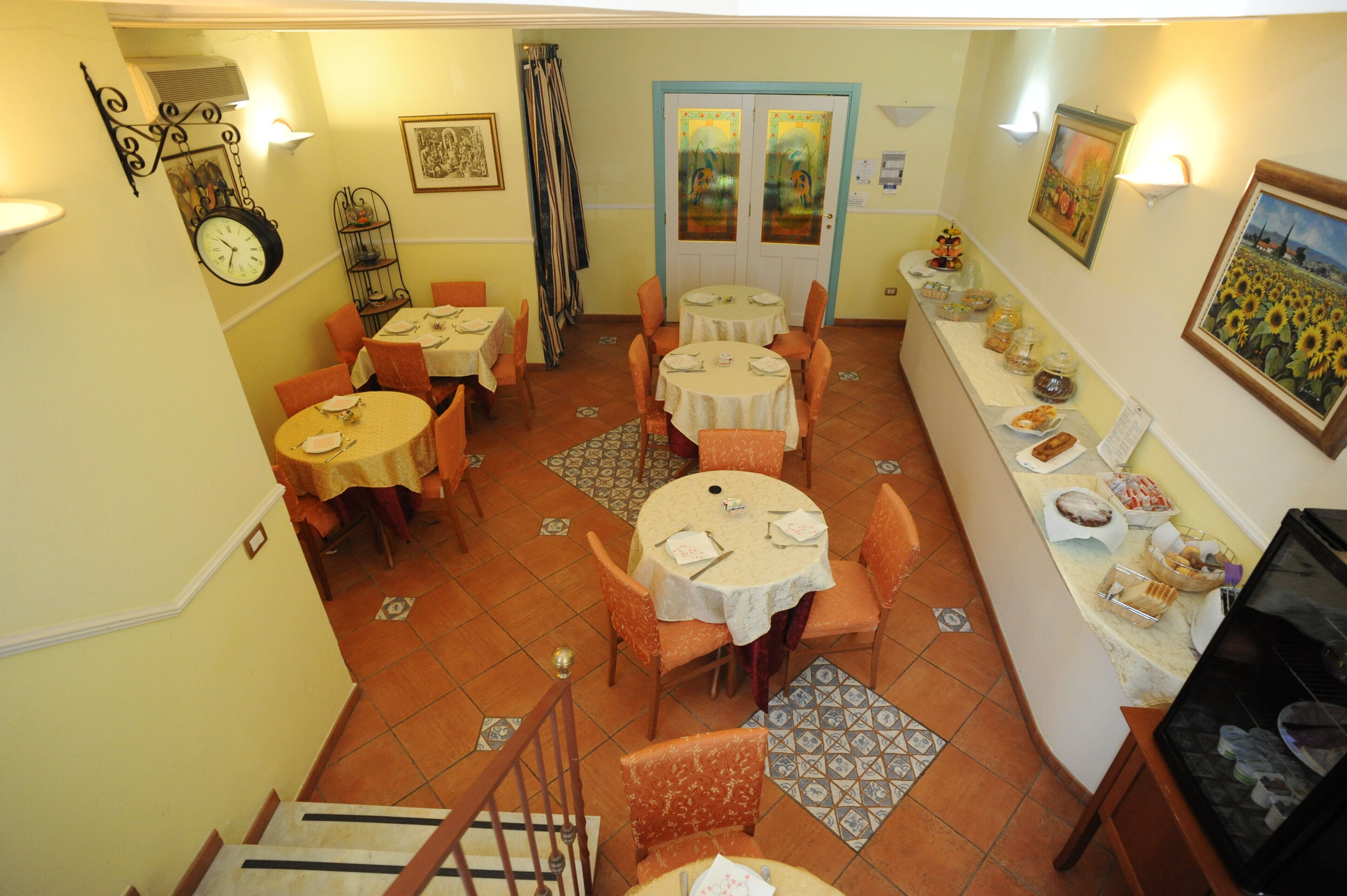A dining area with round tables and orange chairs, a clock, and a counter with food items.