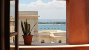 A view from a window with a potted plant, overlooking a body of water and distant land. - Hotel Mediterraneo (Syracuse)