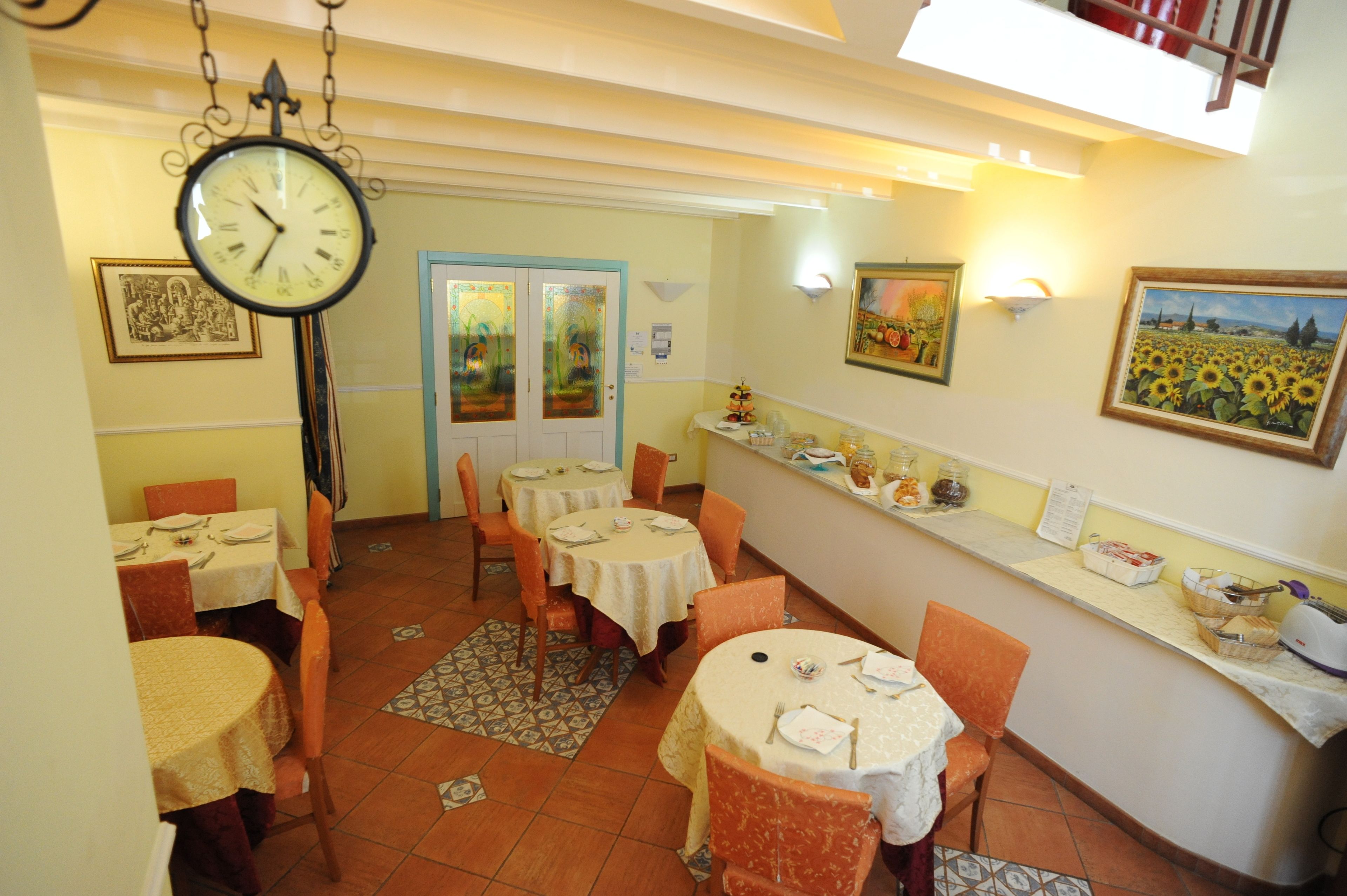 A dining area with tables set for two, a hanging clock, and wall-mounted artwork.