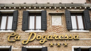 Eine Gebäudefassade mit der Beschriftung "Cà Dogaresca" in goldener Schrift, versehen mit drei Sternen oberhalb des Namens und zahlreichen Fenstern mit schwarzen Rollläden.