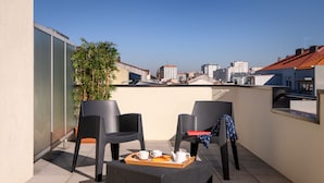 A rooftop terrace with two black chairs, a wicker ottoman, and a tray with a croissant, coffee cup, and teapot. - TRYP by Wyndham Porto Centro Hotel (Porto)