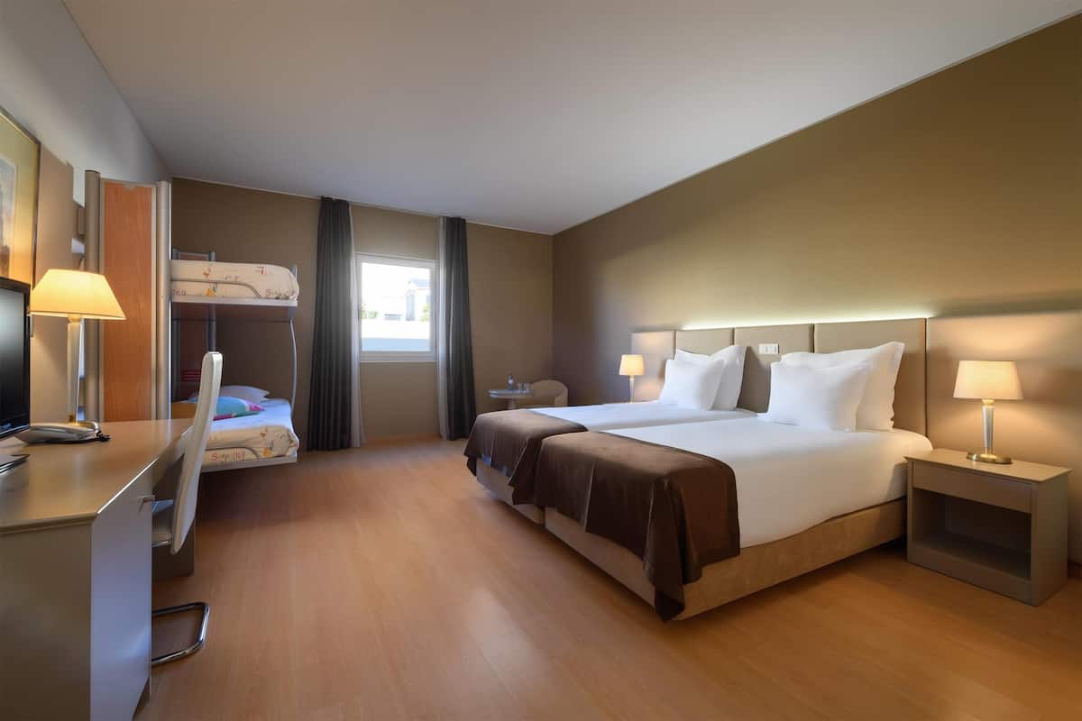 A hotel room with a bed, desk, chair, and a small table.