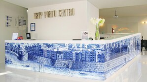Un comptoir d’accueil aux motifs bleus et blancs, une enseigne indiquant « TRYP PORTO CENTRO » et un vase rempli de fleurs blanches.