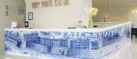A reception desk with a blue and white tiled design, a sign reading "TRYP PORTO CENTRO", and a vase with white flowers.