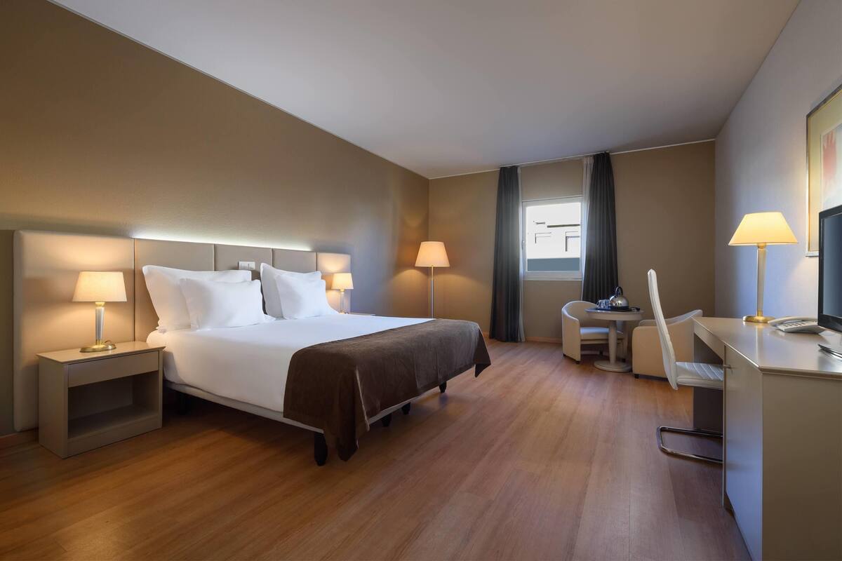 A hotel room with a bed, bedside tables, a desk, and a chair.