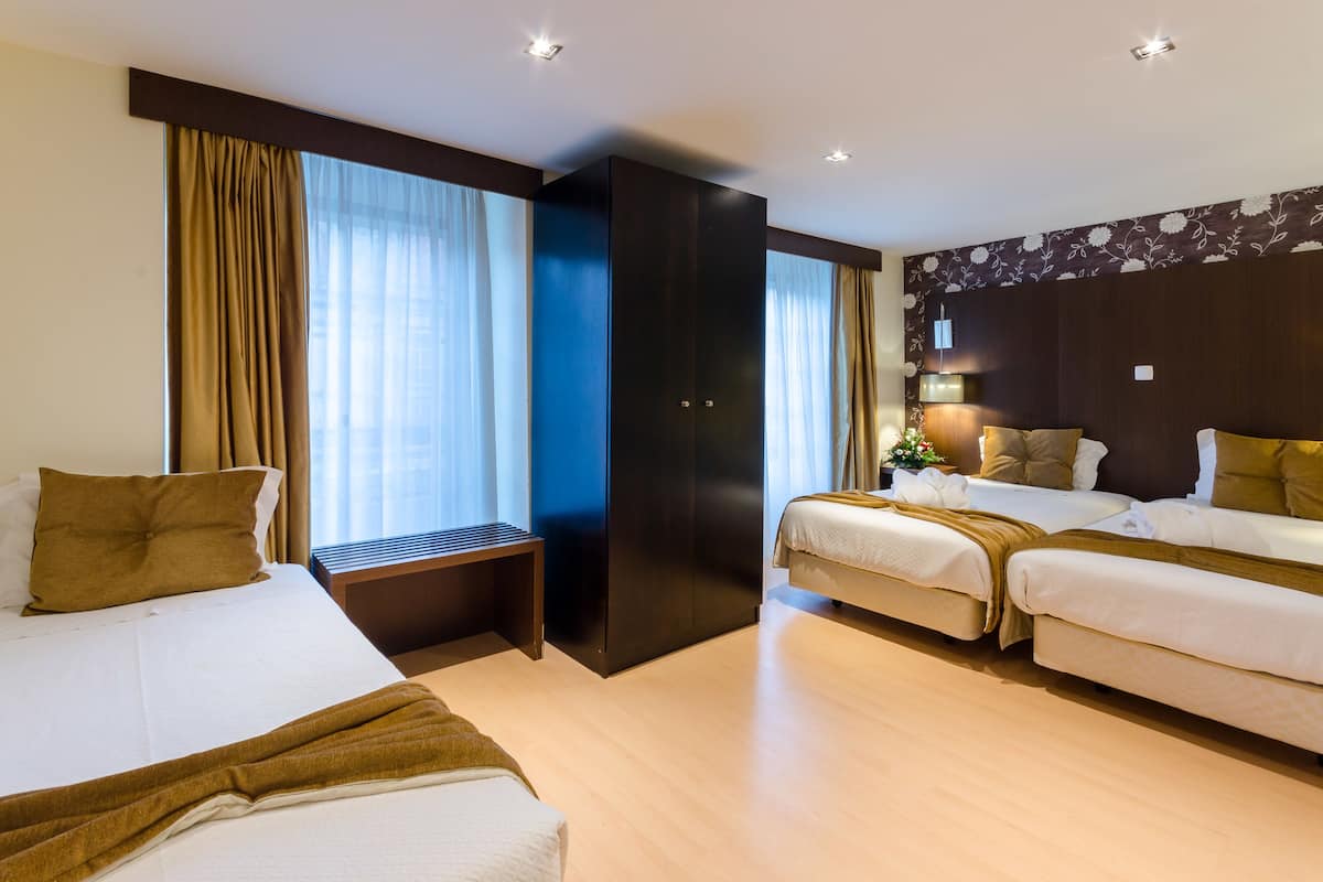 Een hotelkamer met twee bedden, een grote kledingkast, een bankje en een klein tafeltje.
