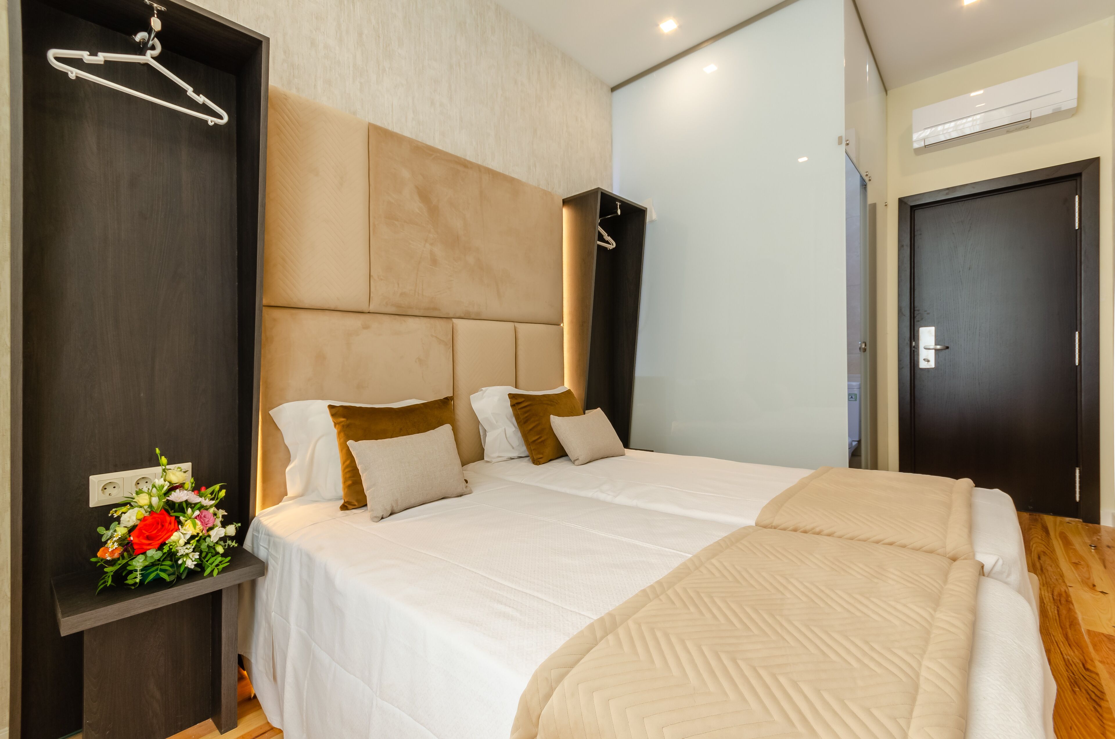 Une chambre d’hôtel avec un grand lit, une table de chevet agrémentée d’un arrangement floral, une armoire et une porte.