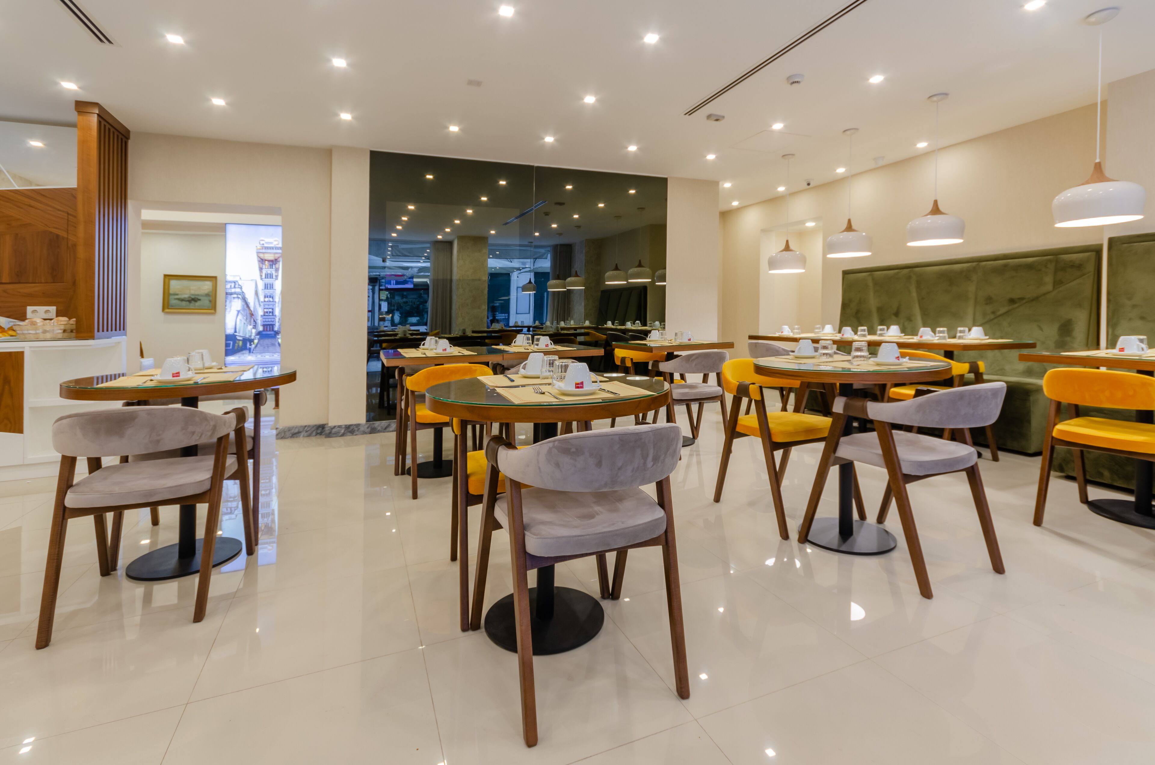 A modern restaurant with round tables and chairs, a wooden counter, and a view of the city through large windows.
