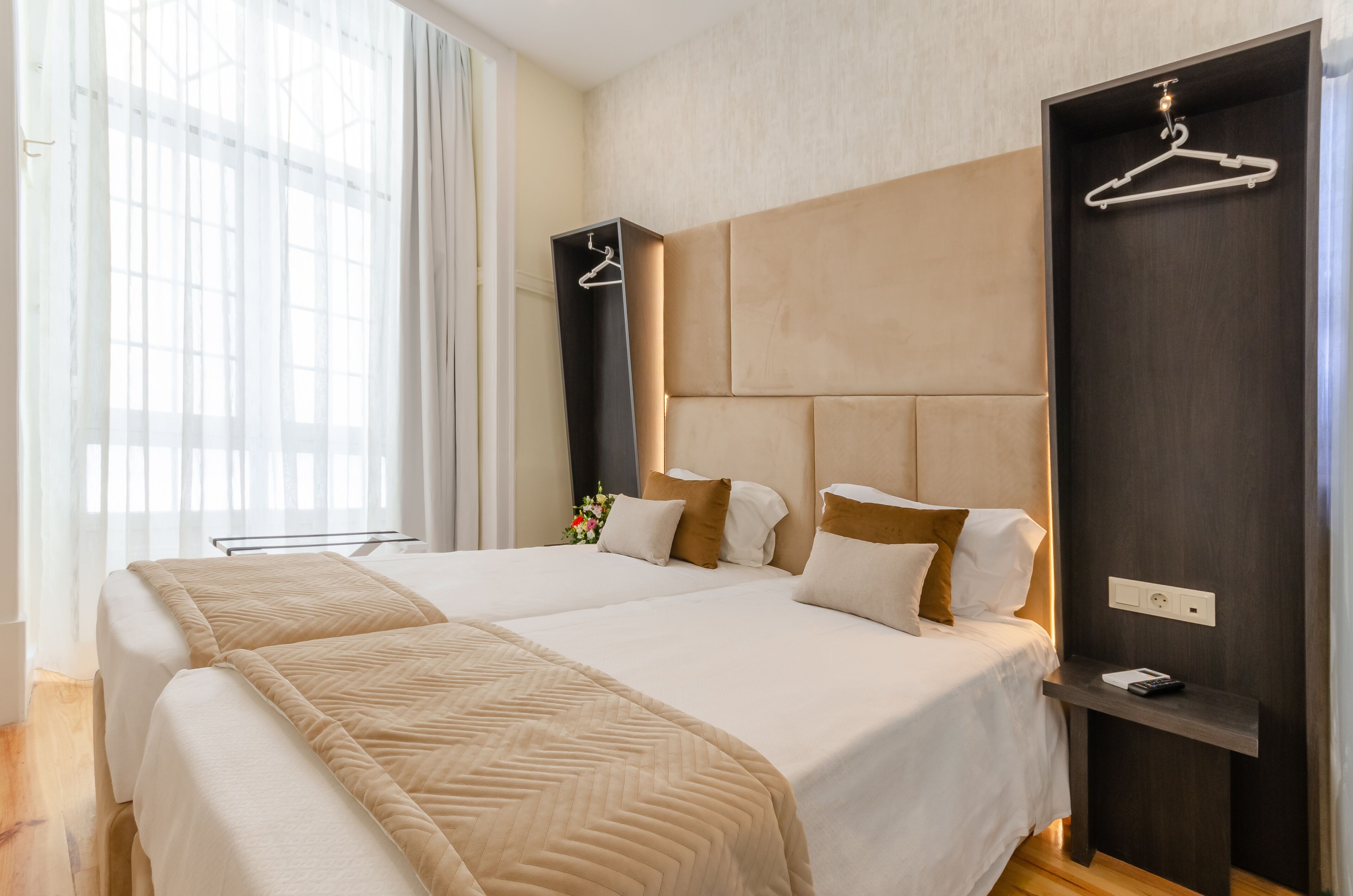A double bed with a beige bedspread, a nightstand with a remote control, and a wooden headboard.