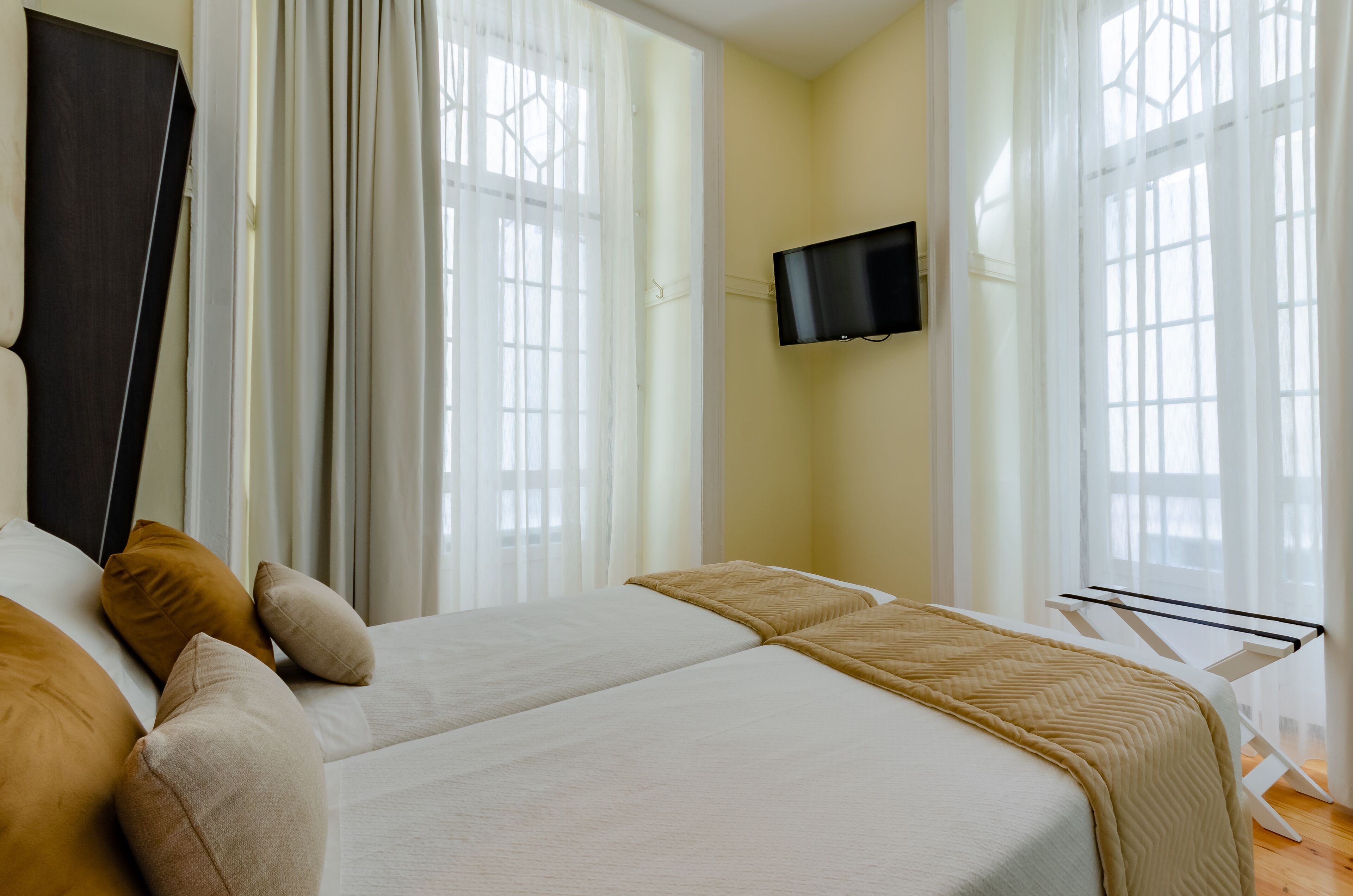 Habitació d'hotel amb dos llits, un televisió de pantalla plana penjada a la paret i finestres grans amb cortines translúcides.