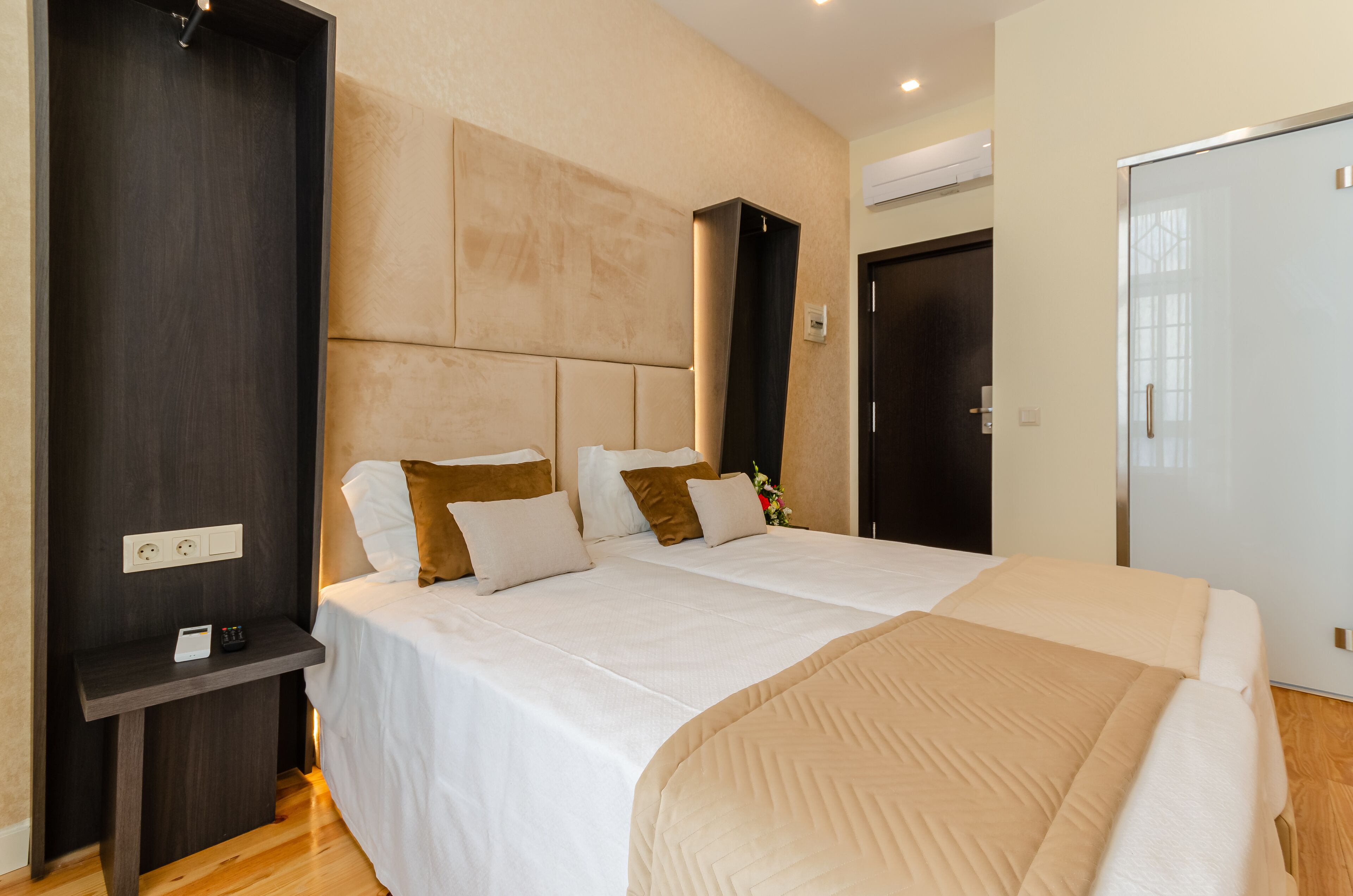 A modern hotel room with a large bed, a bedside table, and a wardrobe.