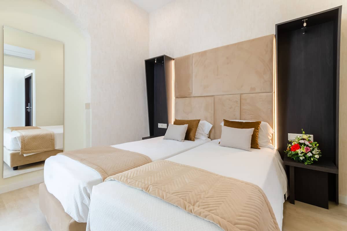 Een hotelkamer met twee bedden, een grote spiegel en een nachtkastje met een bloemstuk.