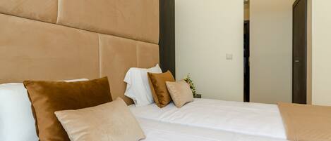 Una habitación de hotel moderna con una cama grande, varios almohadones y una mesita auxiliar.