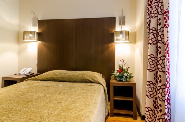 Una habitación de hotel con una cama grande, dos mesitas de noche, un teléfono y una planta decorativa.