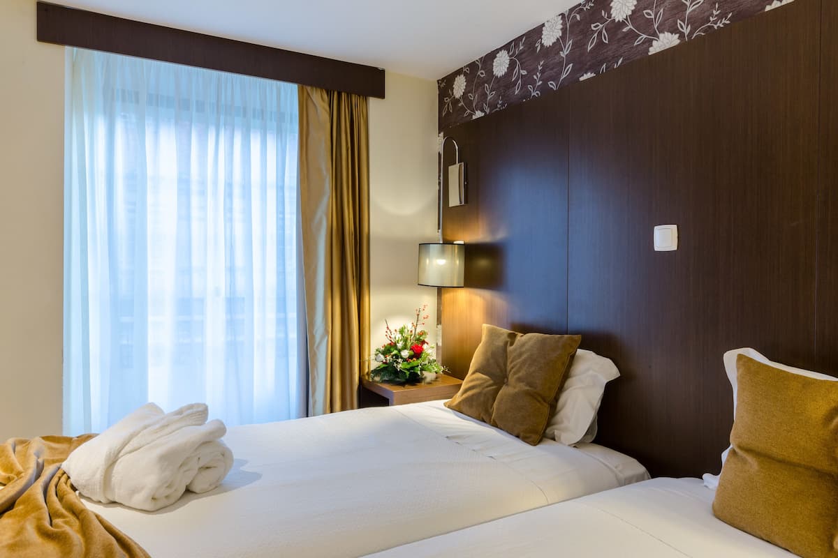 Een hotelkamer met een net opgemaakt bed, een nachtkastje met een lamp en een raam met gordijnen.