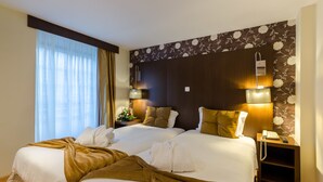 Una habitación de hotel con dos camas, una mesita de noche con lámpara y un papel tapiz estampado con motivos florales.