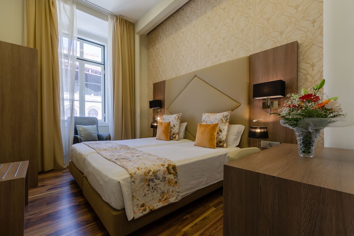 A hotel room with a large bed, two bedside tables, a desk, and a window with curtains.