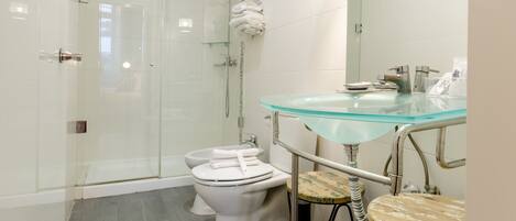 A modern bathroom with a glass shower enclosure, a toilet, and a glass sink with a metal stool.