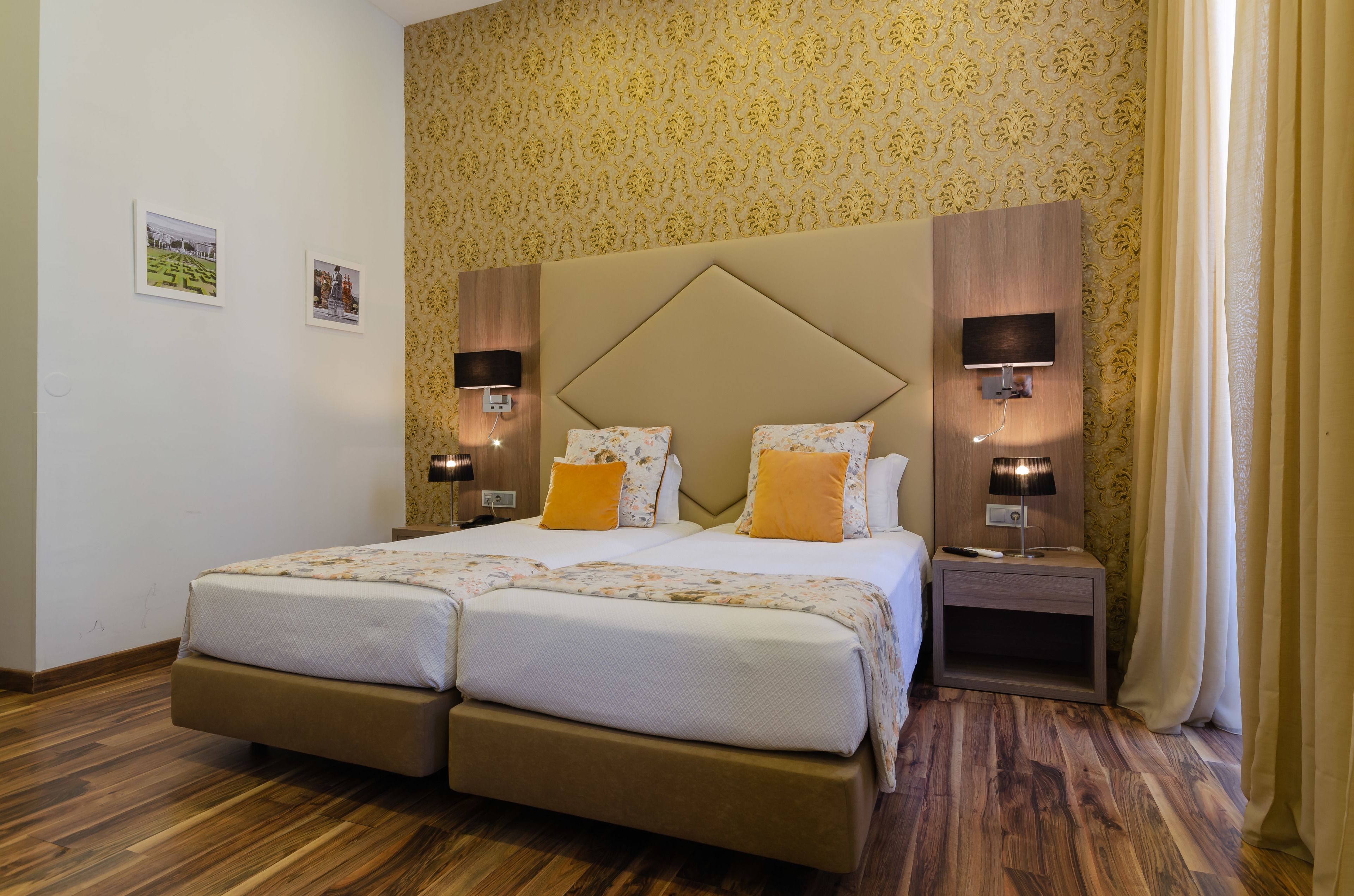 Una cama doble con cabecera de madera, dos mesitas de noche con lámparas, un papel tapiz con estampado floral y suelo de madera.