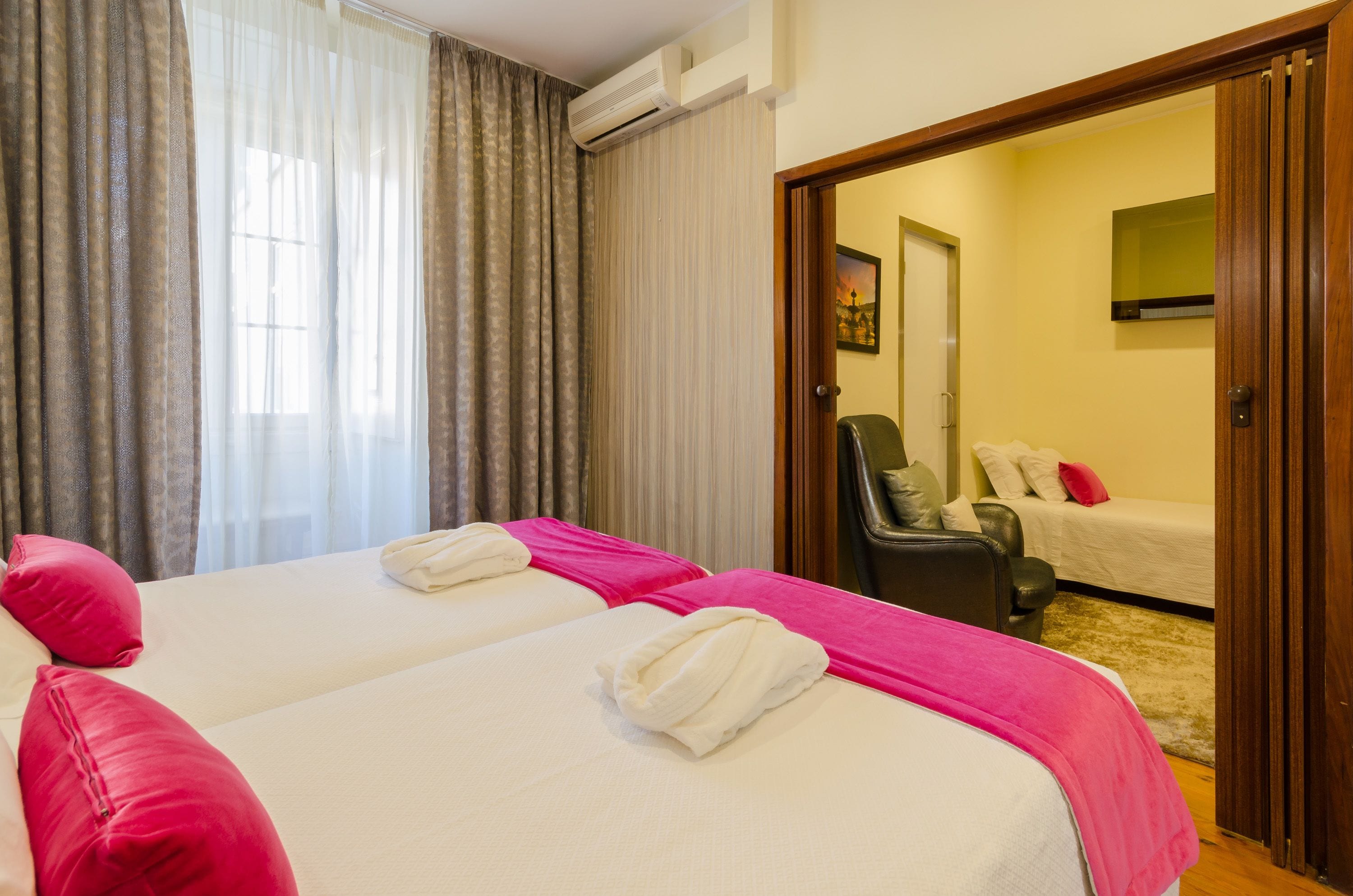 A hotel room with two beds, a chair, a sofa, and a door leading to another room.