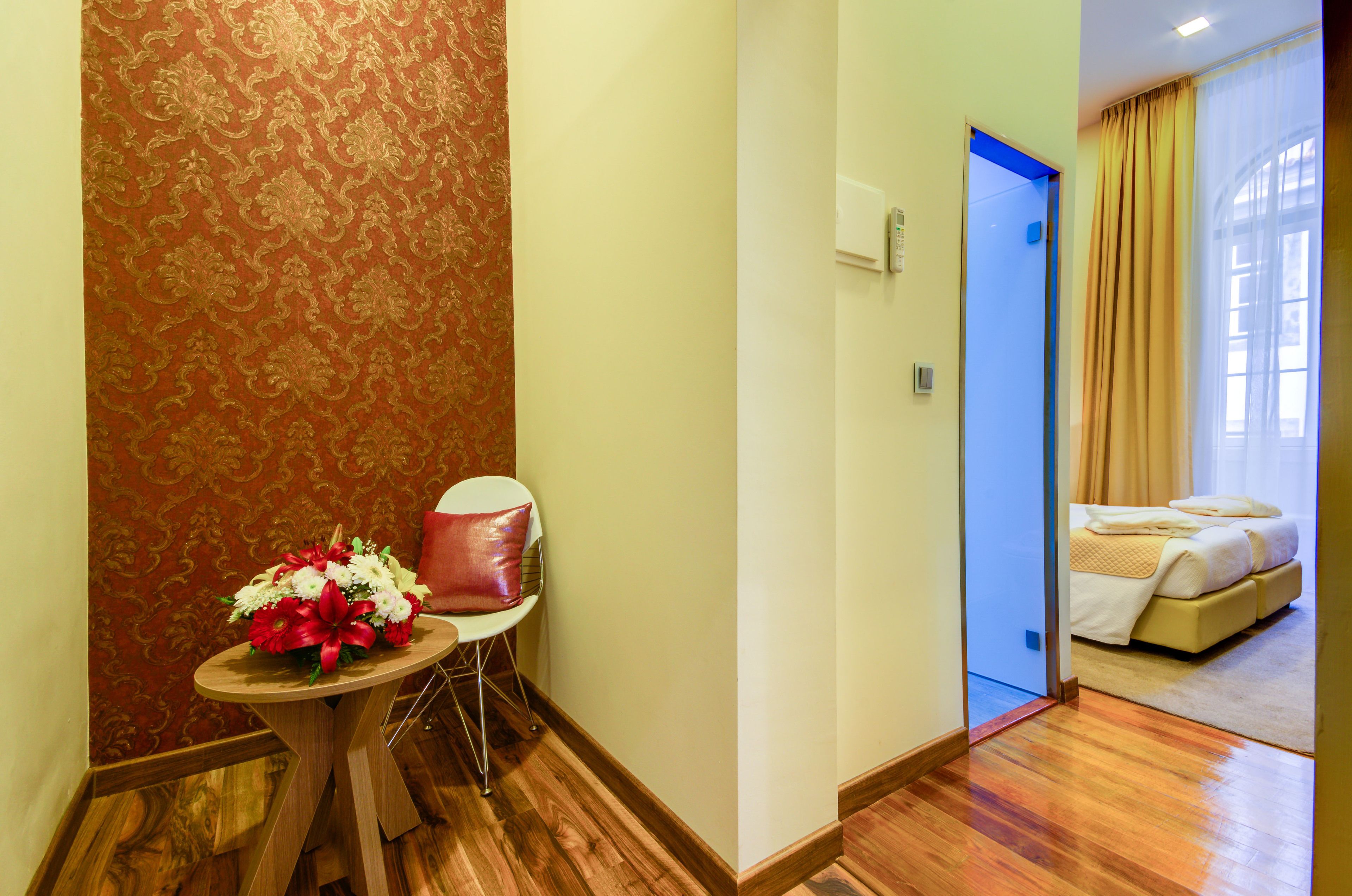Quarto de hotel com uma cama, uma mesinha com um arranjo de flores e uma cadeira.
