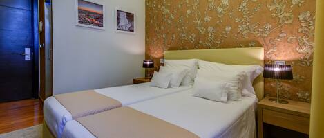 A double bed with a beige headboard, two bedside tables with lamps, and a floral wallpaper pattern on the wall.