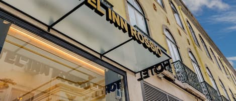 A hotel sign with the name "HOTEL INN ROSSIO" and a reflection of a building facade.