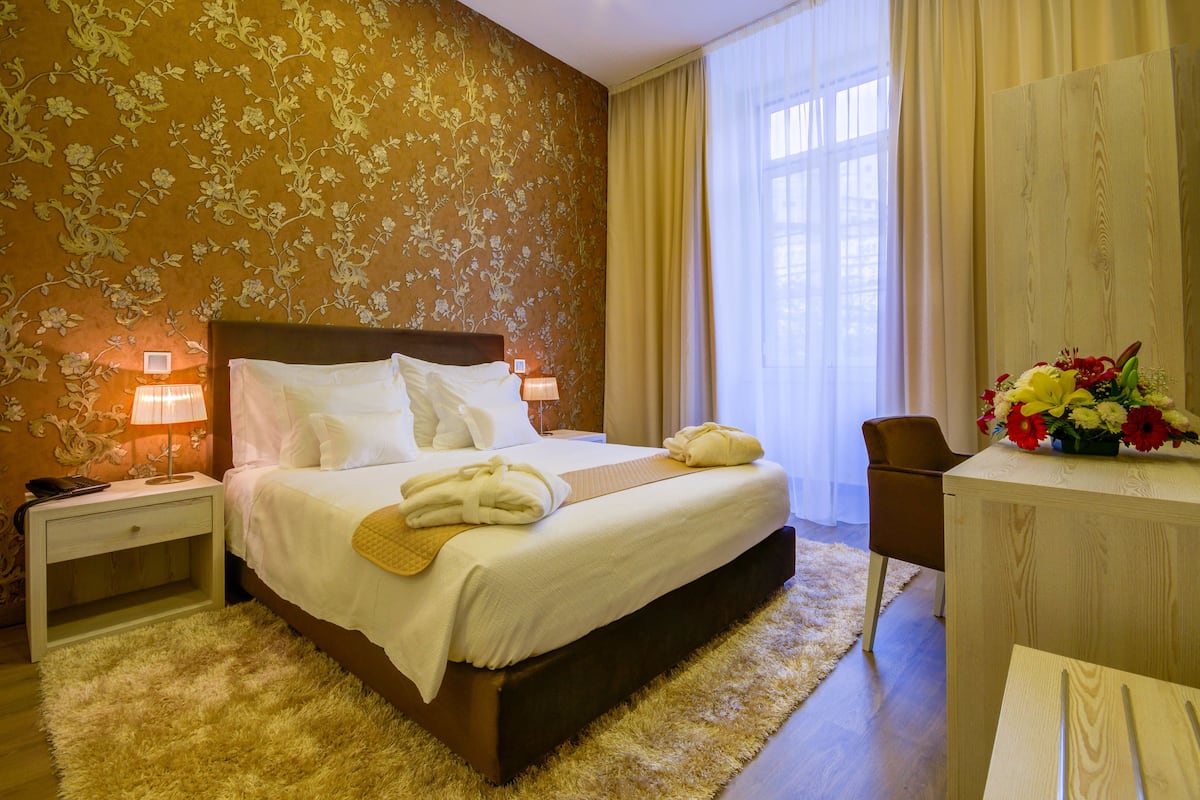 A hotel room with a large bed, a nightstand with a lamp, a wooden desk, and a chair.