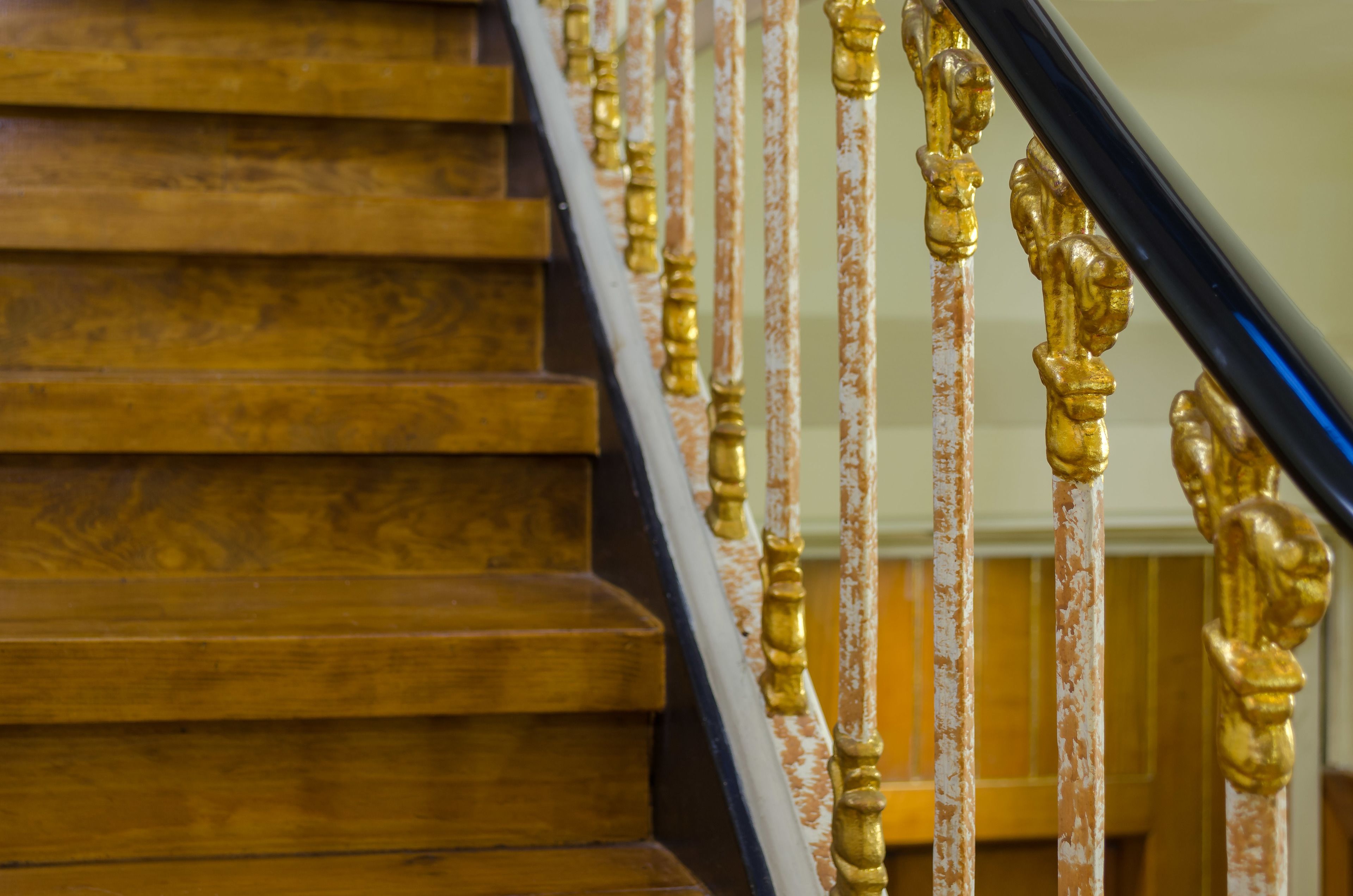 A wooden staircase with ornate golden balusters and a black handrail.