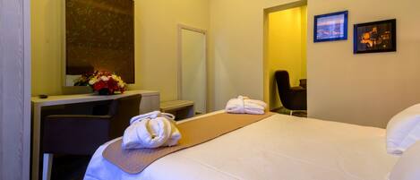 A hotel room with a bed, a desk, a chair, a mirror, and two framed pictures on the wall.