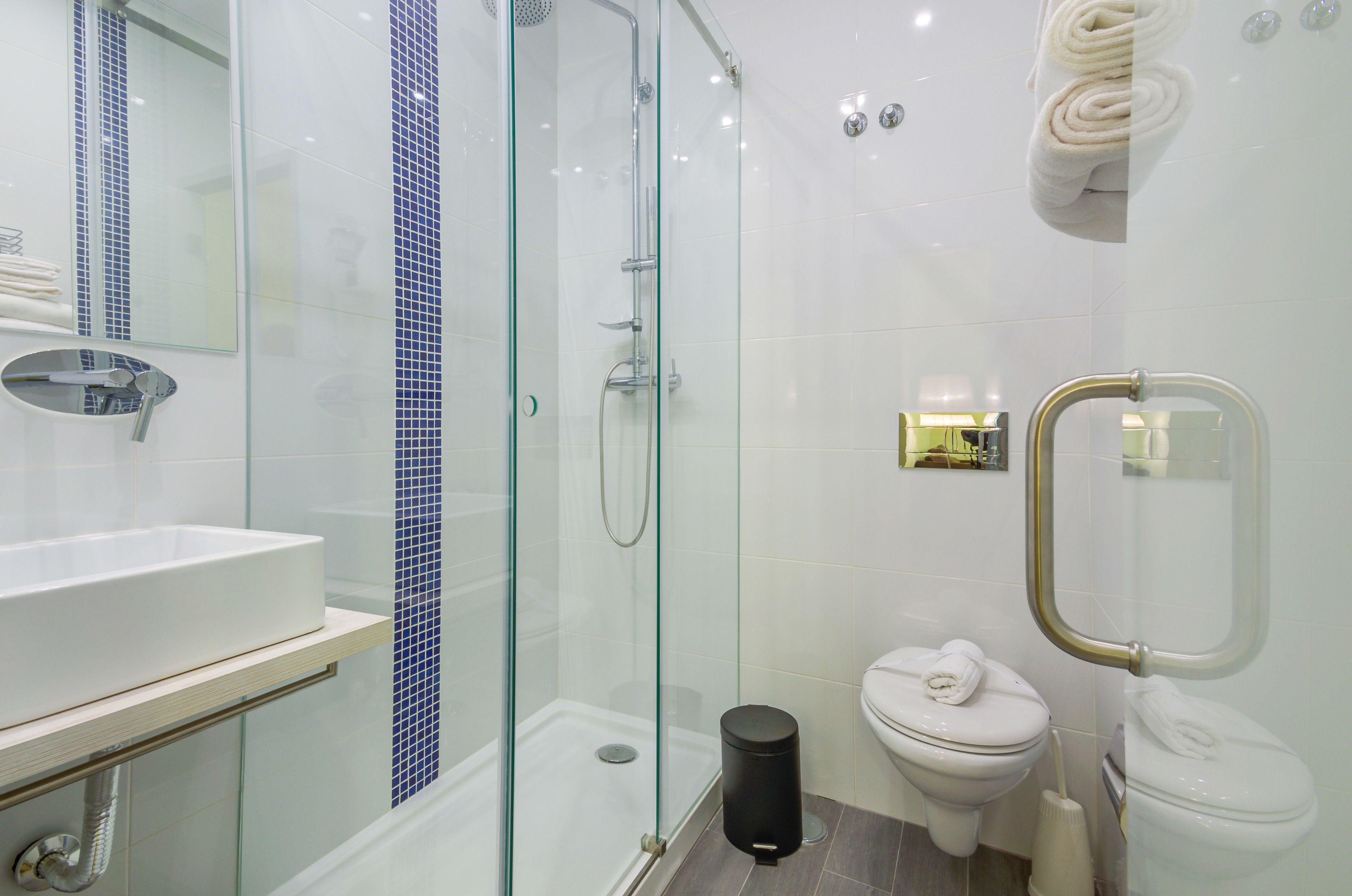 A modern bathroom with a glass-enclosed shower, a white sink, and two toilets.