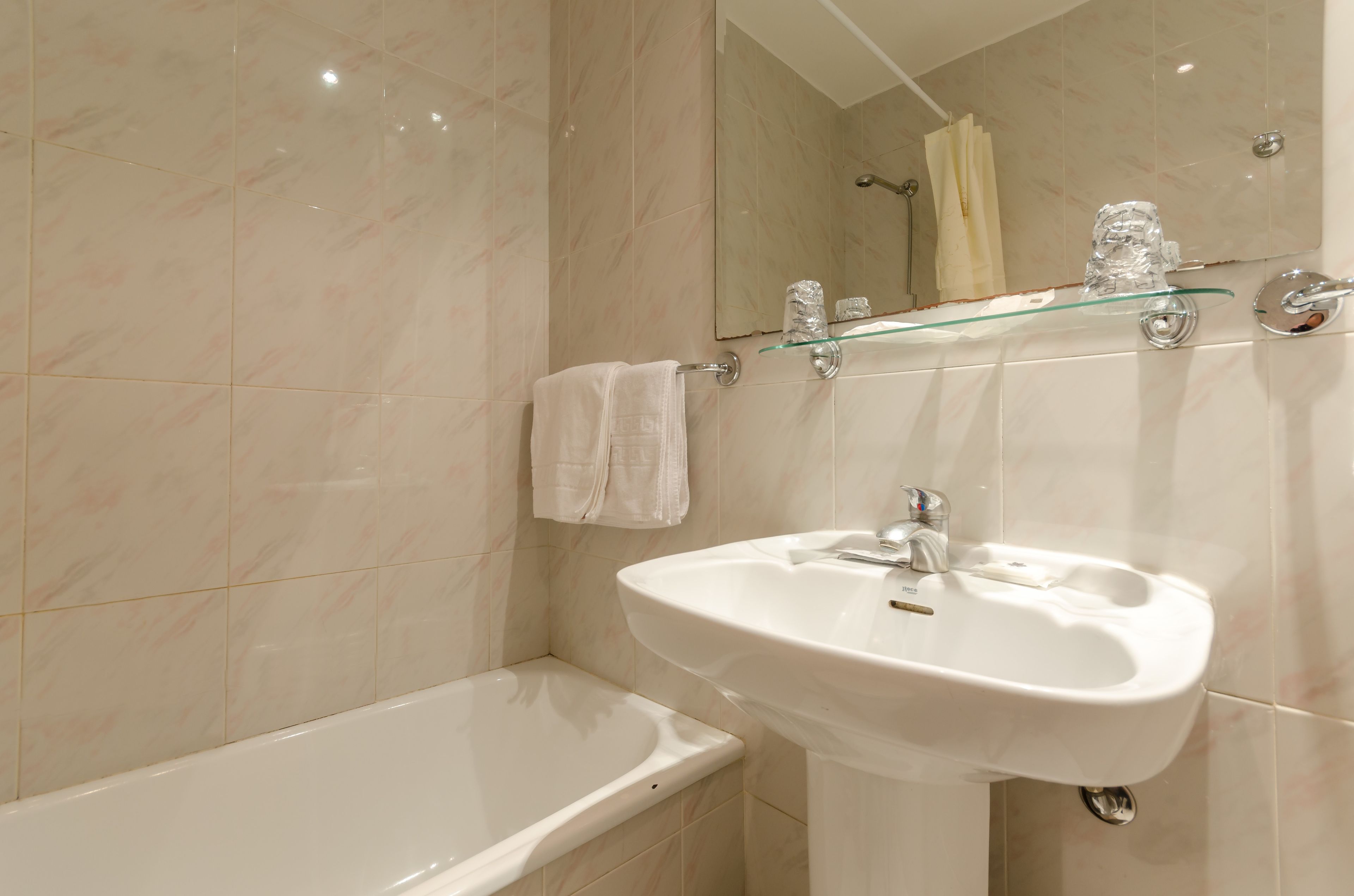 Une salle de bain avec une baignoire blanche, un lavabo blanc et une étagère en verre au-dessus du lavabo.