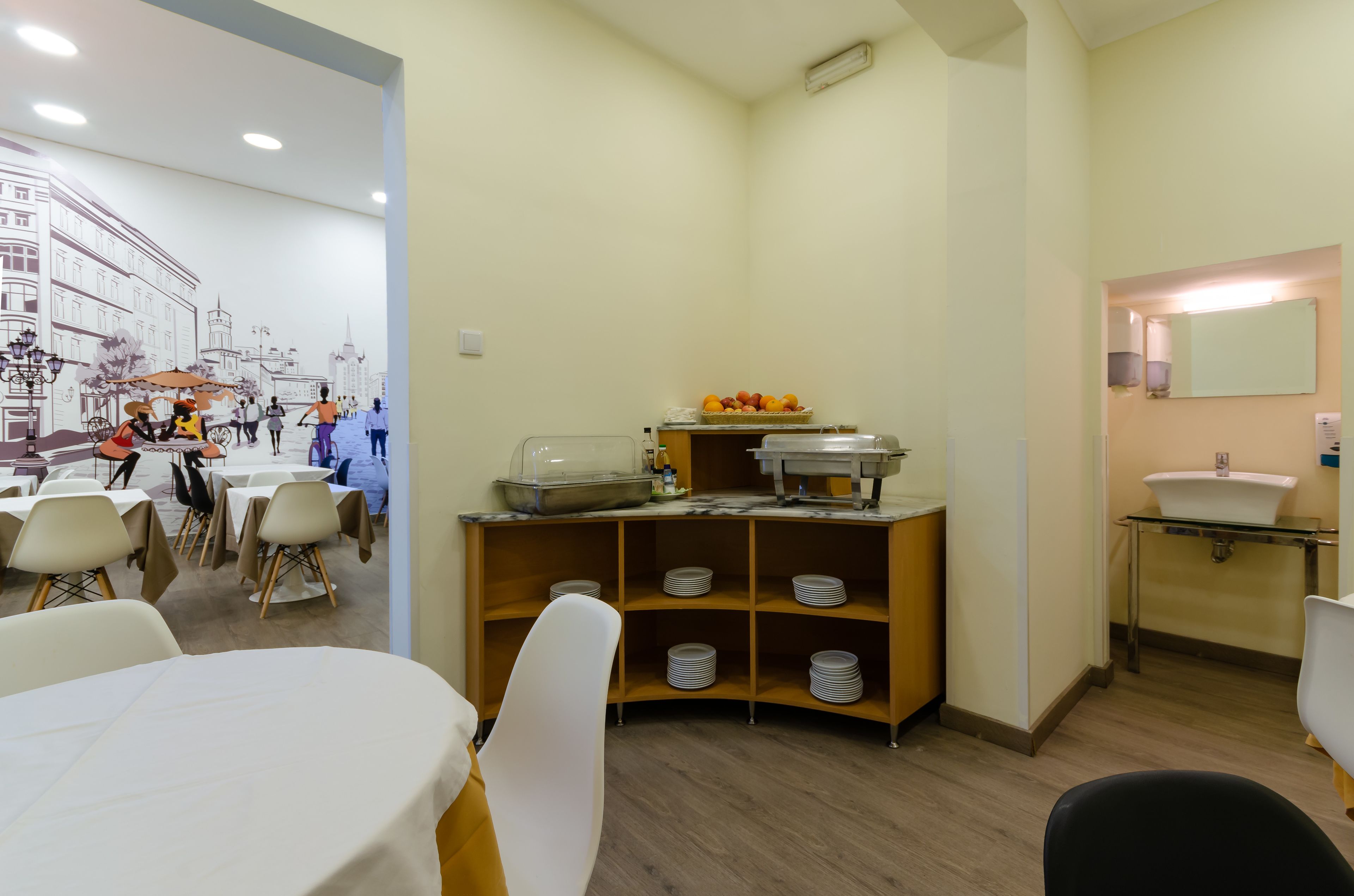 A dining area with tables and chairs, a buffet counter with food and condiments, and a sink with a mirror.