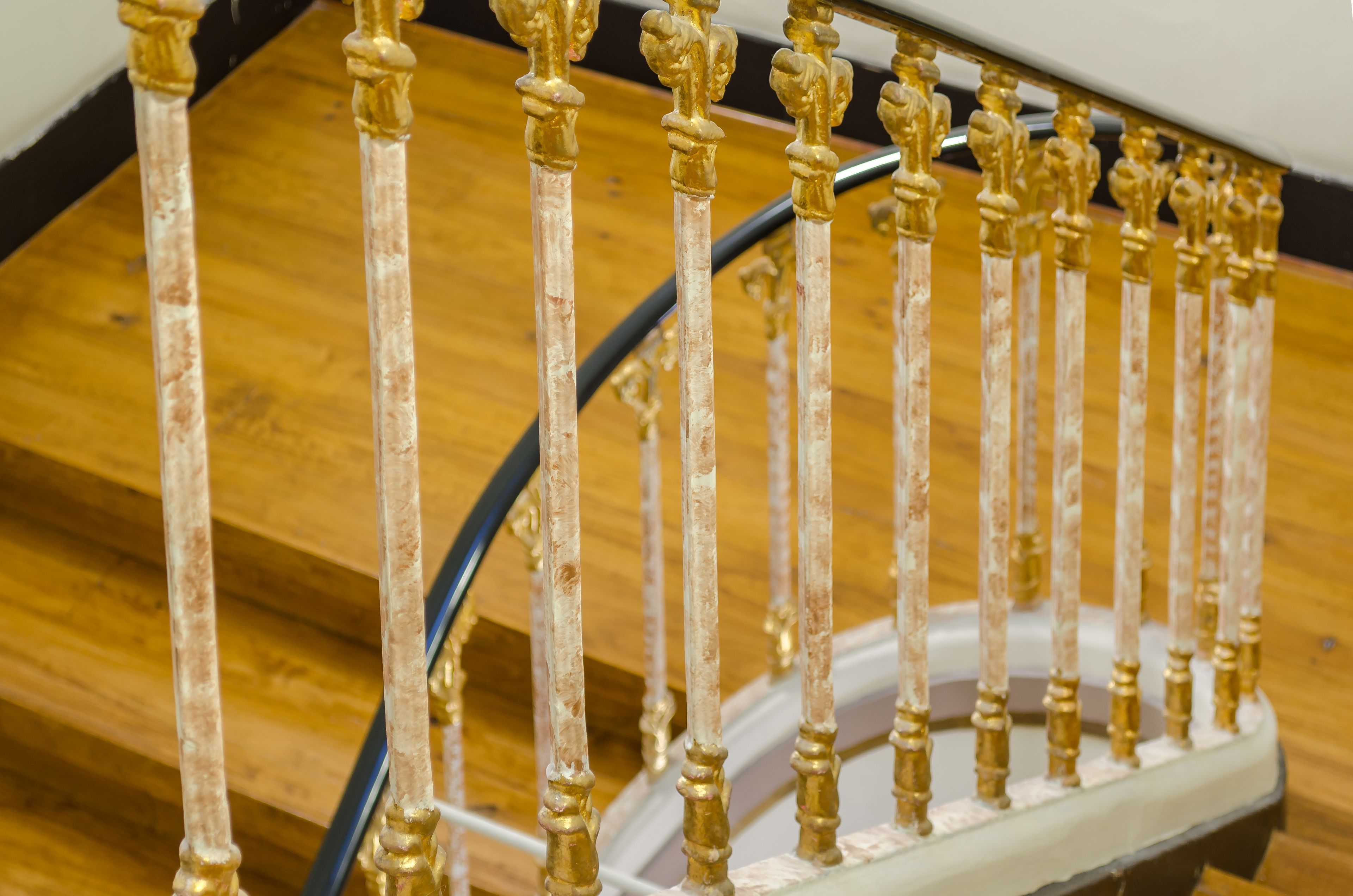 A close-up of a staircase with ornate golden balusters and a white handrail.