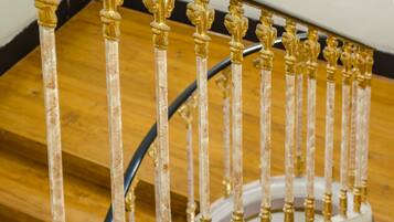 Ein Detailaufnahme einer Treppe mit aufwendig verzierten, goldenen Balustern und einem weißen Geländer.
