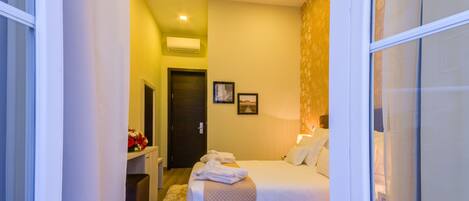 A hotel room with a bed, a bedside table, a nightstand, a wall-mounted air conditioner, and a door.