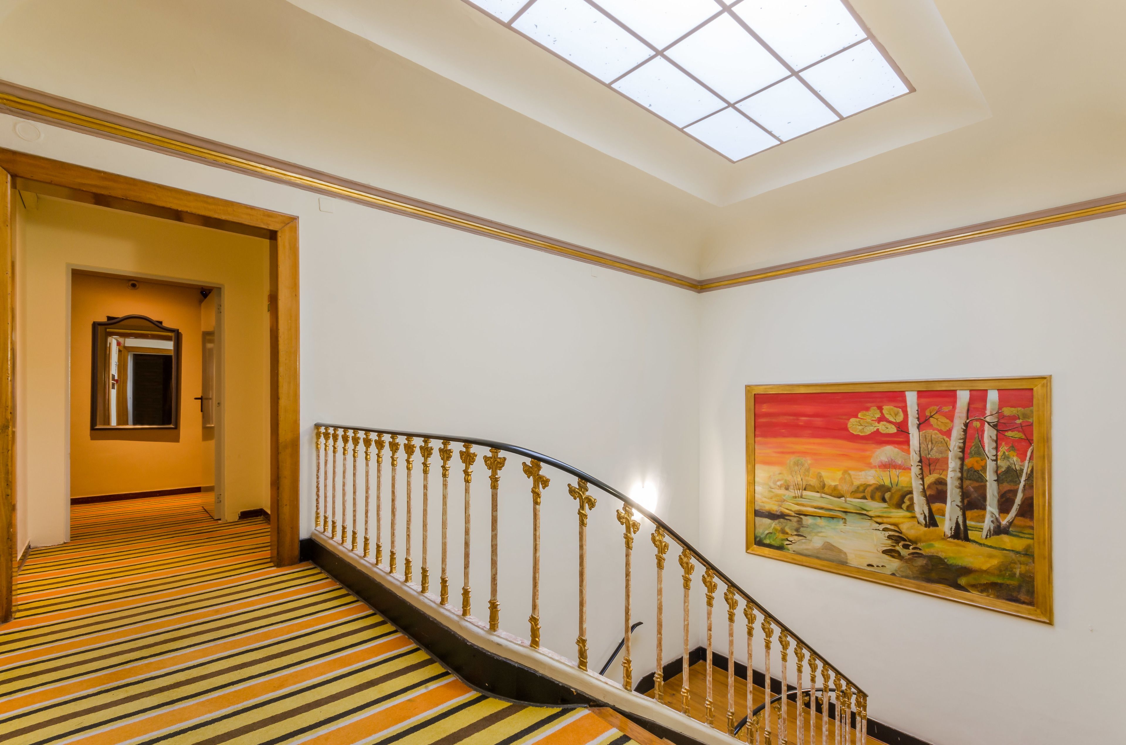 Een trap met een gestreept tapijt en een schilderij van een landschap aan de muur.
