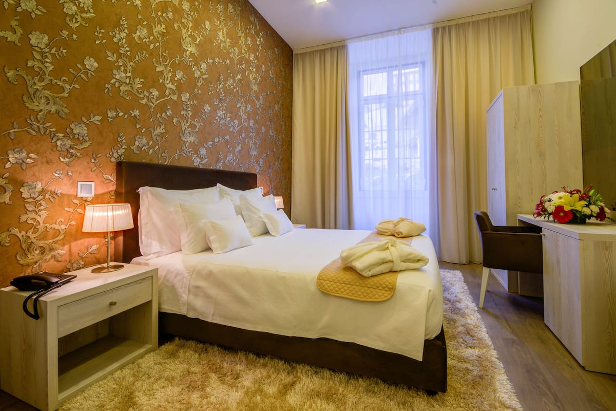 A hotel room with a bed, bedside table, lamp, and a desk with a chair.