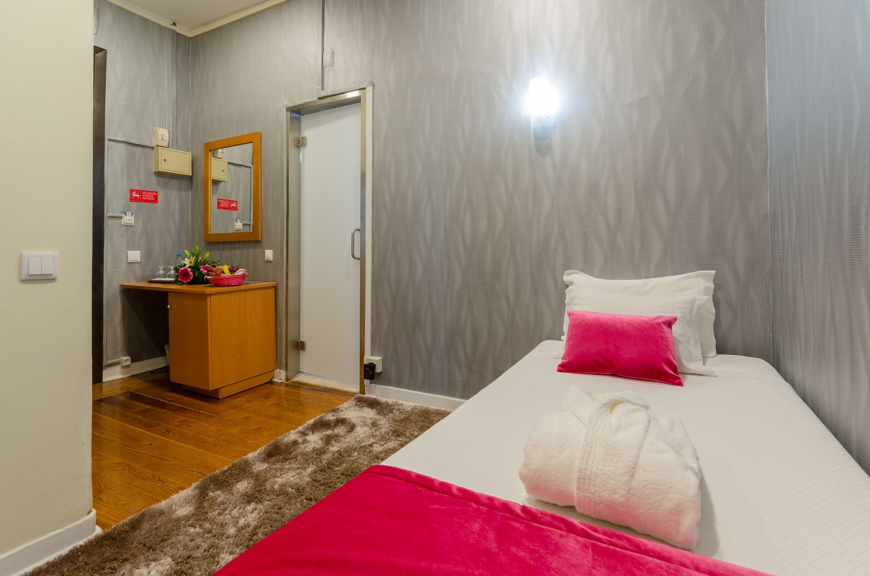 A hotel room with a bed, a small wooden dresser, a mirror, and a door leading to another room.