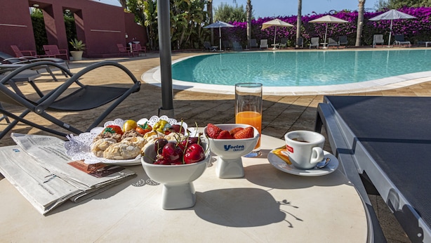 Desayuno junto a la piscina con periódico, frutero, jugo y café.