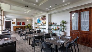 Un comedor moderno con varias mesas y sillas, una cocina al fondo y plantas decorativas.