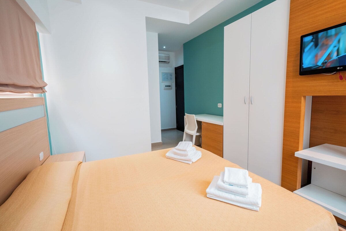 Habitación de hotel con cama, televisor montado en la pared, escritorio y silla.