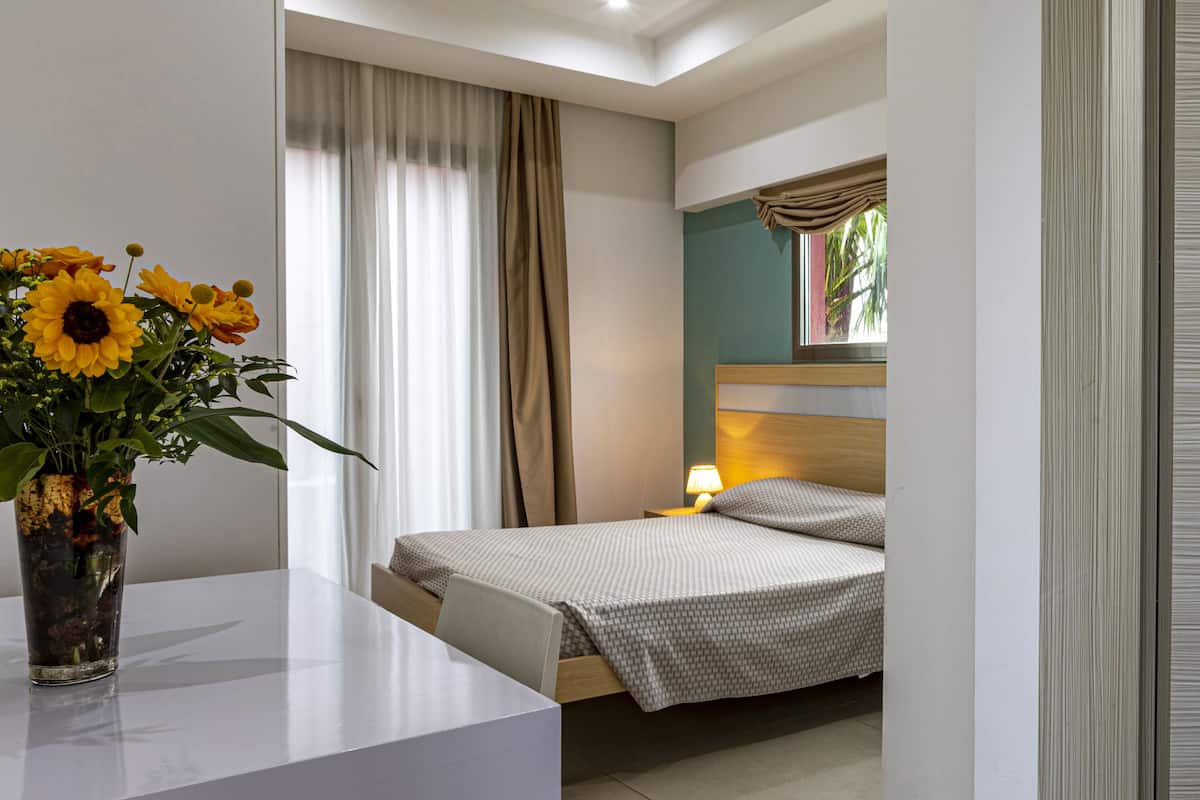A hotel room with a bed, bedside table, lamp, and a vase with flowers.