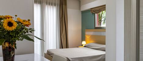 A hotel room with a bed, bedside table, lamp, and a vase with flowers.